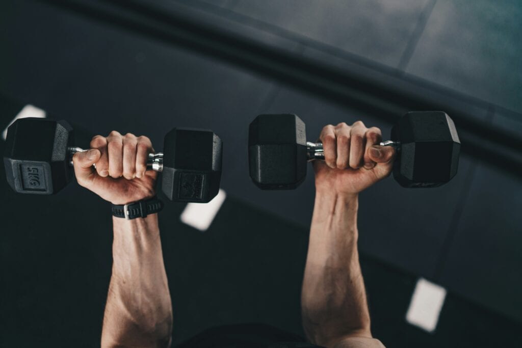 Focused determination: A man lifts free weights, his muscles engaged, showcasing dedication to fitness and strength training.