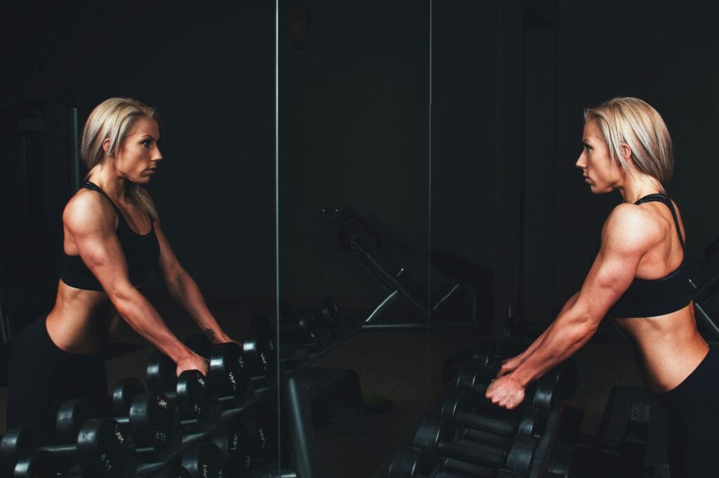 Empowering self-reflection: A woman gazes into the mirror, dumbbells in hand, embodying strength and determination.