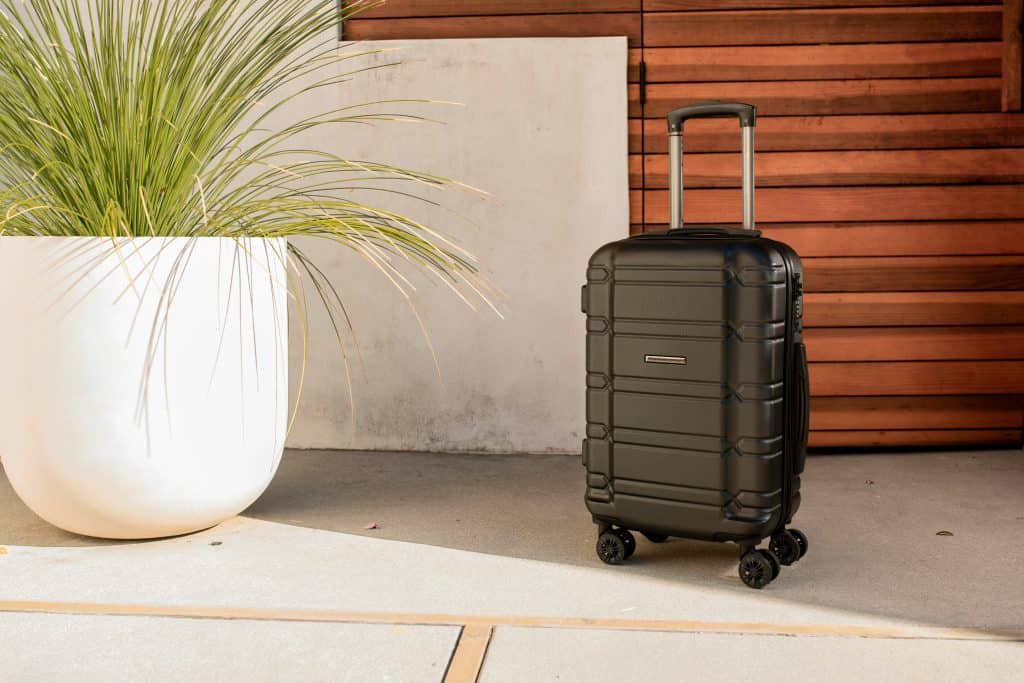 Rolling suitcase standing upright on a sidewalk outside, ready for travel.