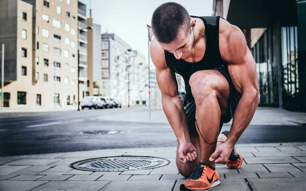 Man in running clothes tying his shoe on the sidewalk, preparing for a run.