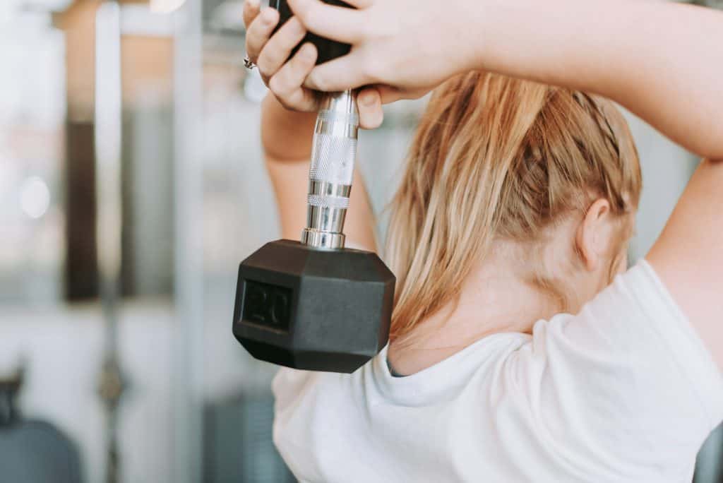 Girl lifting a weight behind her head, performing a tricep workout.