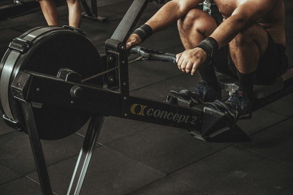 A man intensely focusing while using a rowing machine at the gym, demonstrating a strong, engaged posture and steady rhythm, emphasizing the integration of physical exercise and mindfulness.