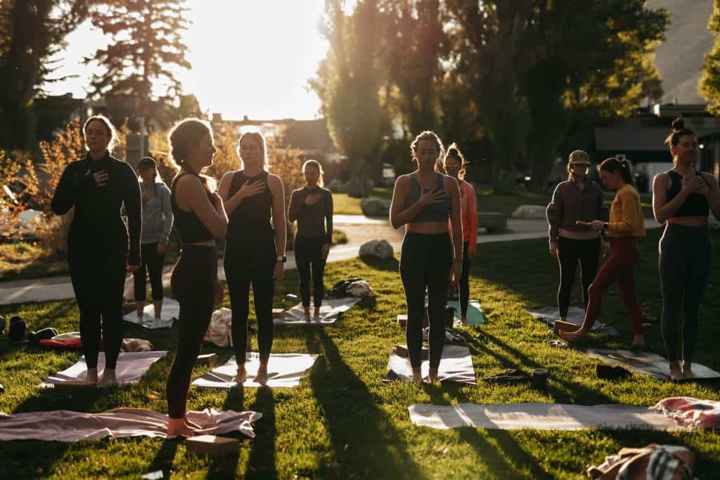 A group of people standing on yoga mats, practicing mindfulness with eyes closed and hands in a meditative pose, reflecting concentration and tranquility in a serene environment.