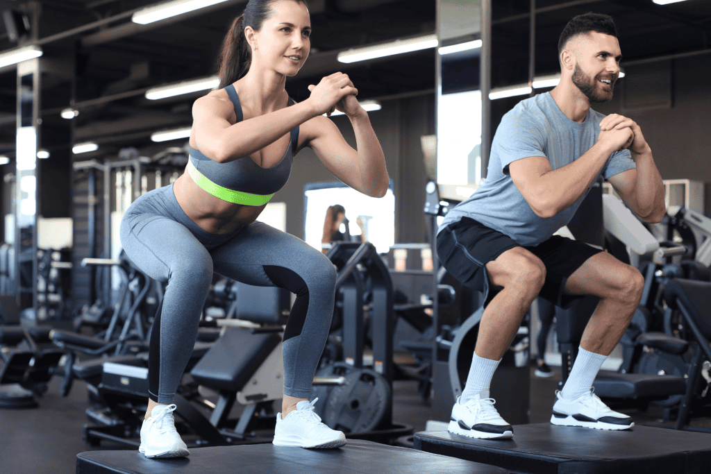 Two young people performing box jumps at the gym, showcasing strength, agility, and high-intensity training in a dynamic fitness environment.