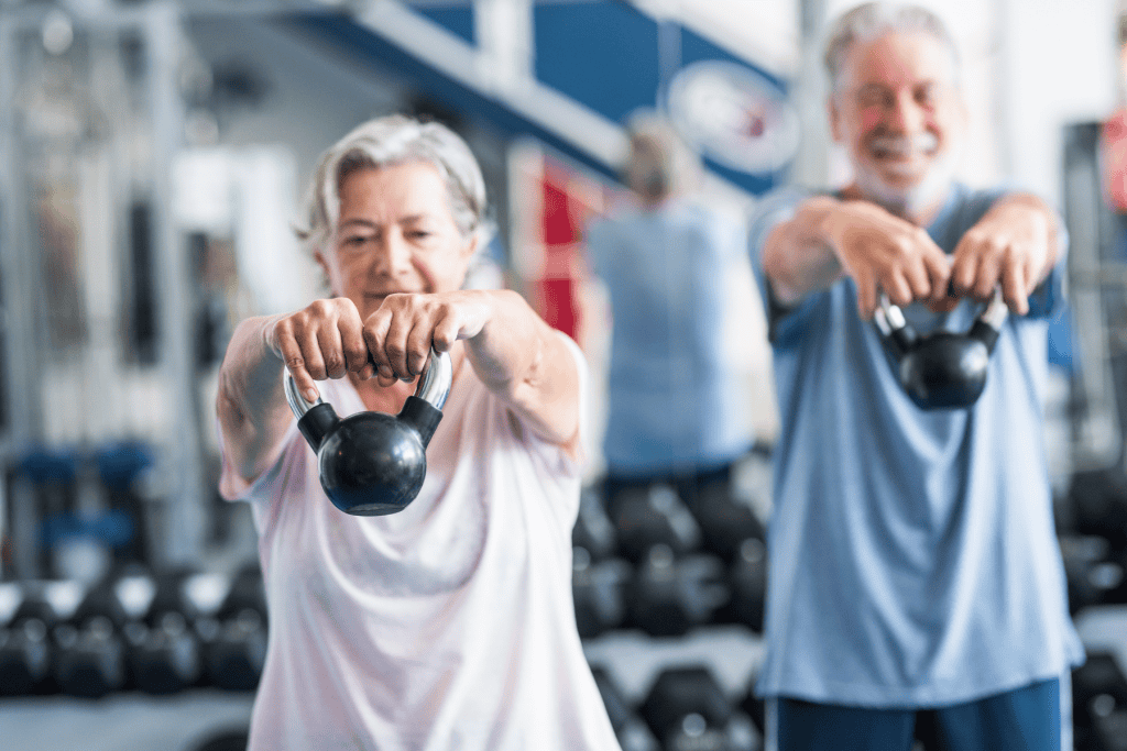 Two senior citizens exercising with kettlebells, demonstrating strength training and active aging in a supportive fitness setting