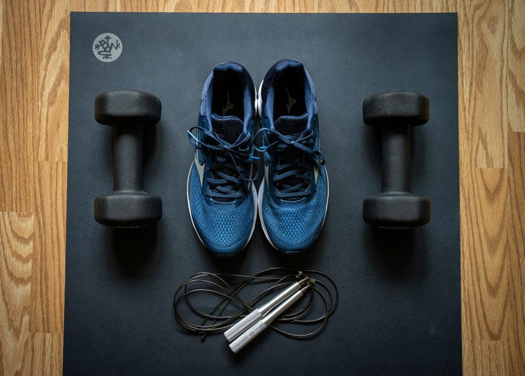 Running shoes, dumbbells, and a jump rope neatly arranged on a yoga mat, representing a well-rounded fitness routine with cardio, strength, and flexibility elements.