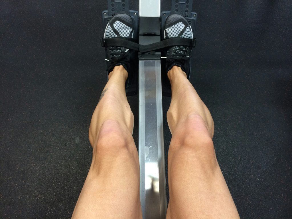 Strong woman rowing on a machine in the gym, highlighting her muscular legs and focused effort during an intense workout.