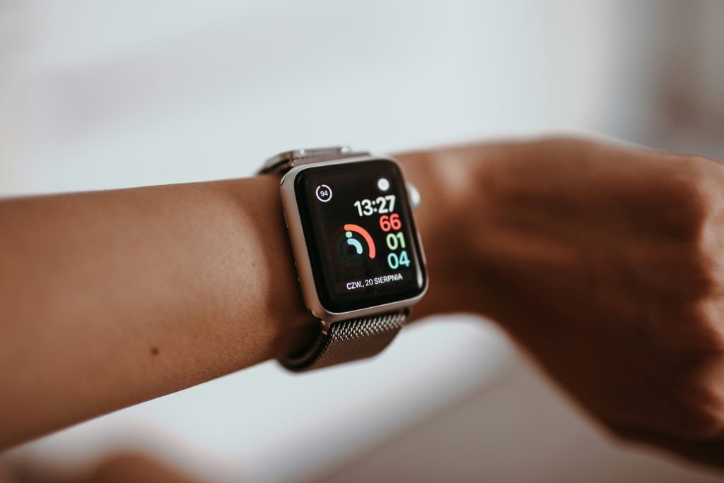 Close-up of a person's wrist wearing a smartwatch displaying fitness metrics, including heart rate, activity progress, and the time. The watch face is brightly lit against a blurred background, emphasizing the fitness tracking features.