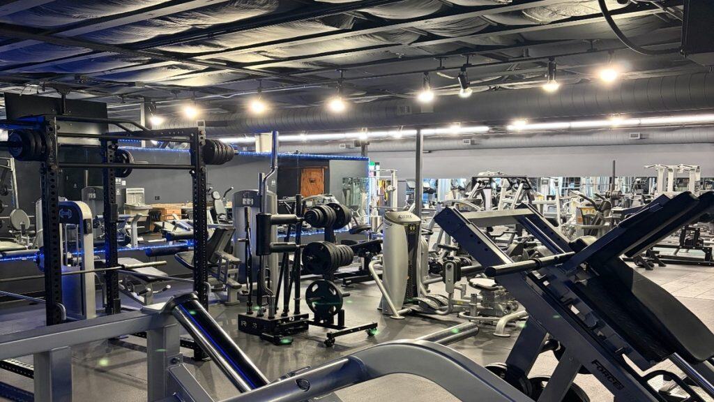 Full gym floor at Peak Fitness SLO showing squat racks, free weights, and strength machines with blue accent lighting