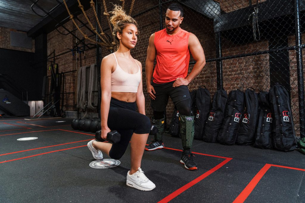 Personal trainer coaching a woman through a dumbbell lunge exercise during a strength training session