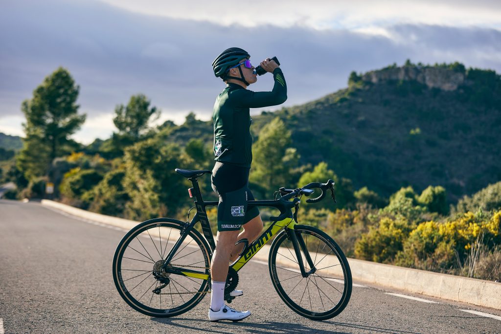 Cyclist drinking from a water bottle during an outdoor workout, illustrating hydration needs during exercise