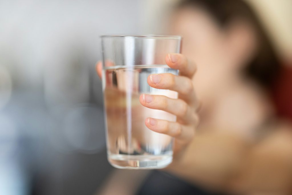 Person holding a clear glass of water, representing daily hydration habits for active adults
