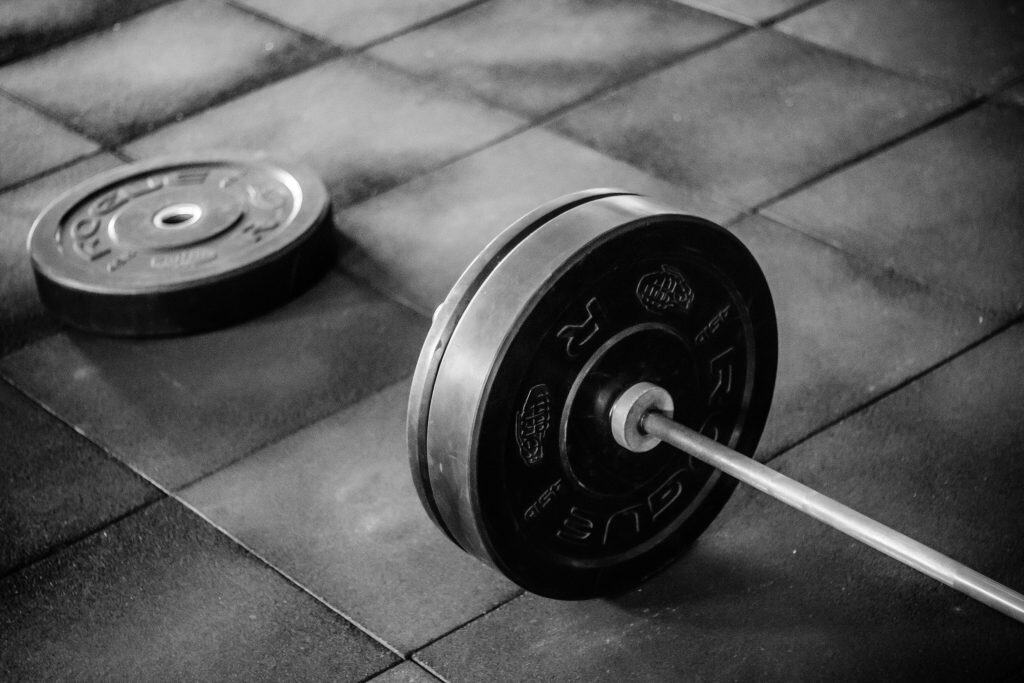 Hands loading a Rogue weight plate onto a barbell in a gym setting