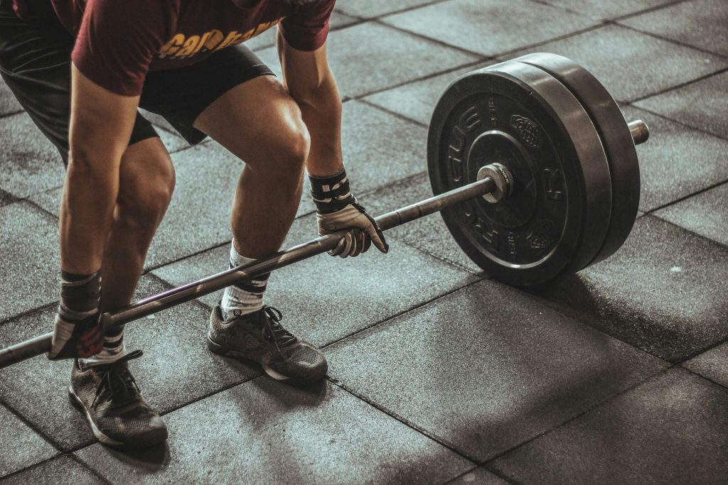 Man lifting loaded barbells resting on a dark gym floor with a clean, minimal aesthetic.