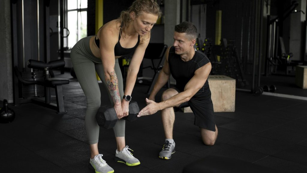 A personal trainer coaching a client through a dumbbell Romanian deadlift at a gym