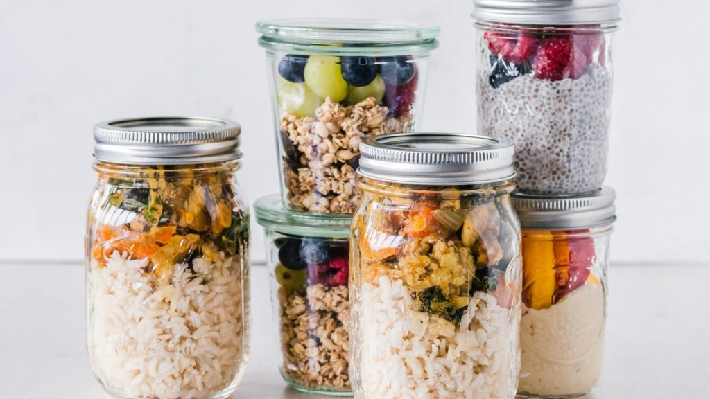 Six glass mason jars filled with prepped healthy meals and snacks for the week
