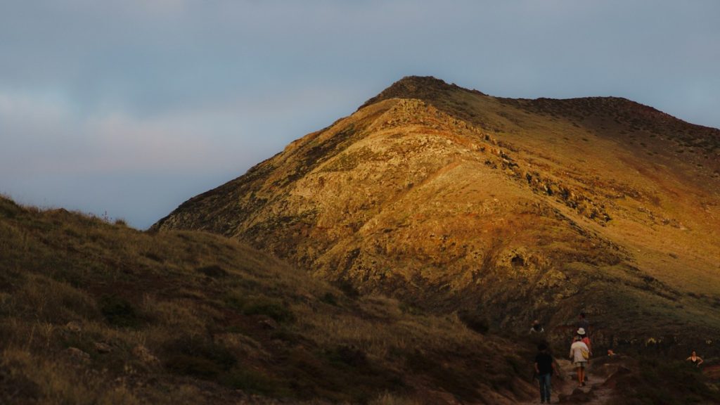 Two hikers ascending a golden grassy hillside trail at sunset