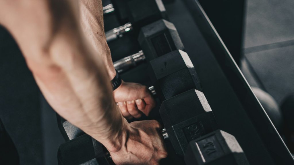 Person reaching for a hex dumbbell off the rack in a clean, well-lit gym