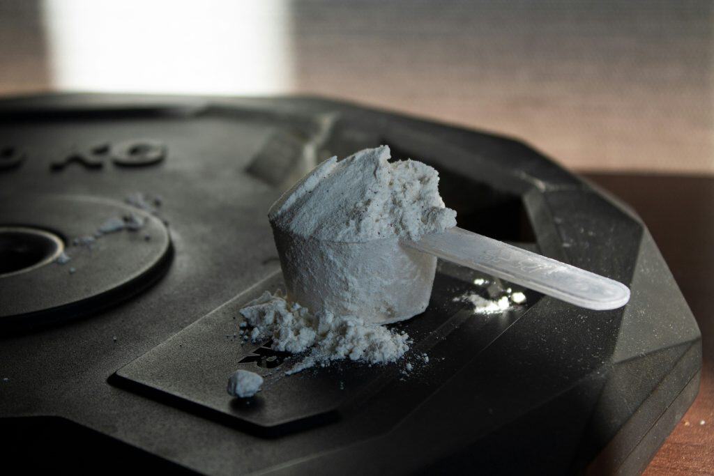 Scoop of creatine monohydrate powder tipped onto a light surface