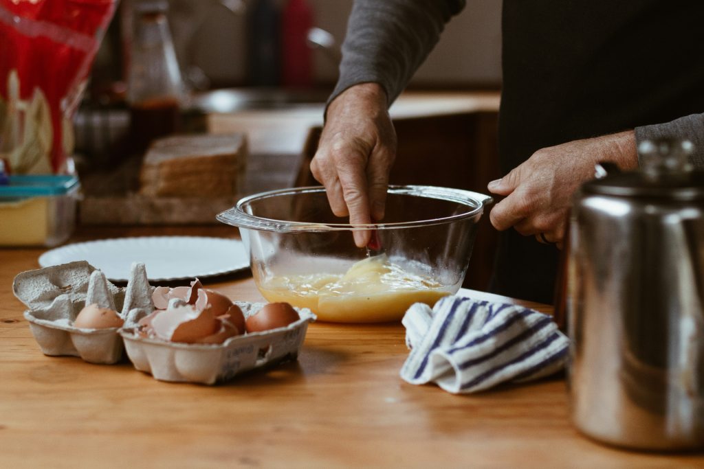 hands cooking a fresh meal in a kitchen with eggs, coffee, and bread on the counter