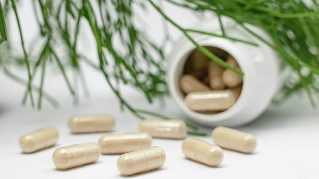 Supplement capsules spilling from a white bottle onto a light surface