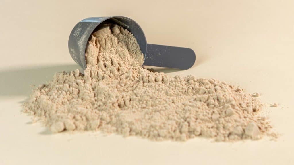 Scoop of creatine monohydrate powder tipped onto a light surface