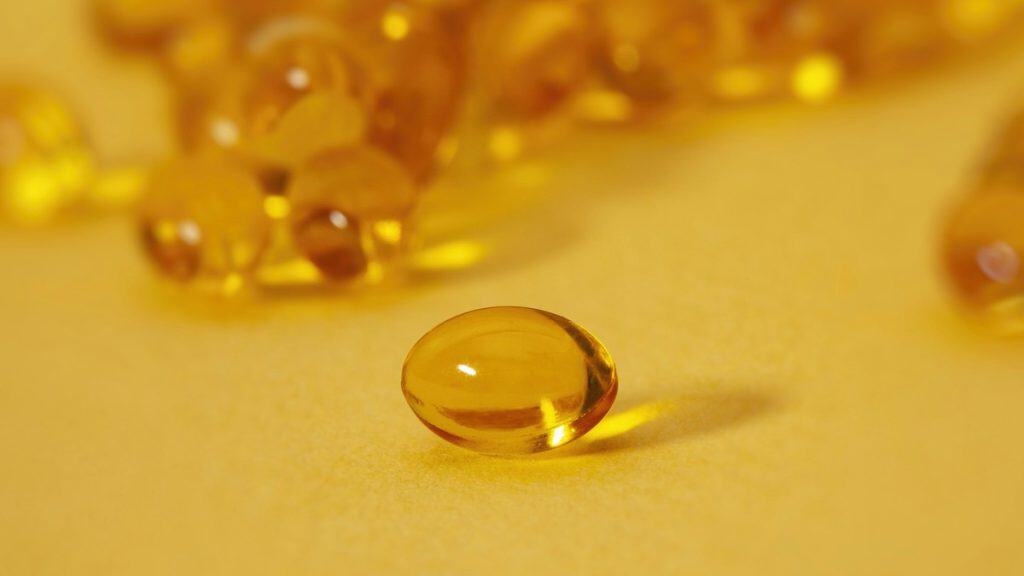 Golden omega-3 fish oil softgel capsules on a yellow background