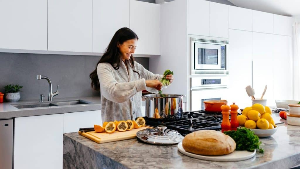Woman cooking a fresh meal in a bright kitchen with vegetables, citrus, and bread on the counter