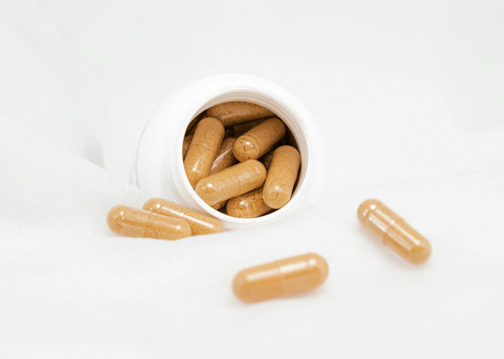 Supplement capsules spilling from a white bottle onto a light surface